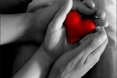 Two pairs of hands holding a red felt heart