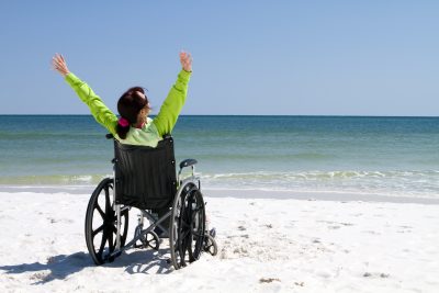 Woman with arms raised celebrates her achievement and success in the sunshine in a wheelchair.