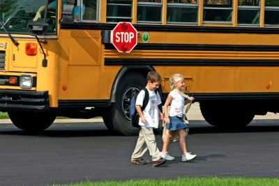 Two children crossing the street in front of a school bus